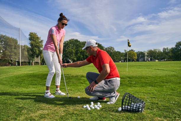 Focused dark-haired beginner lady golfer practicing a proper grip technique assisted by her male instructor