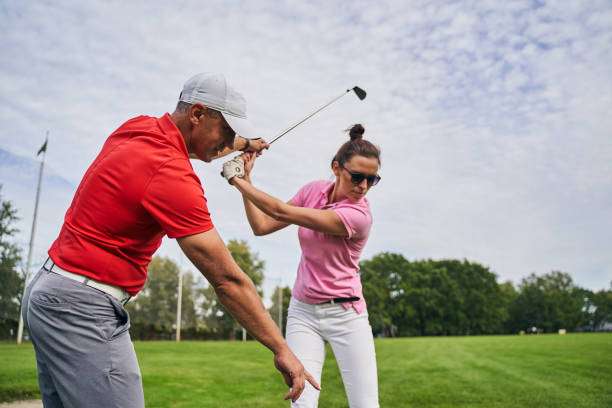 Focused young woman golfer holding a mid-iron over her head helped by her personal trainer