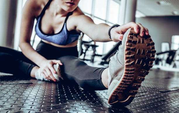 Image of gorgeous young fitness woman sitting in gym near window while make stretching exercises.